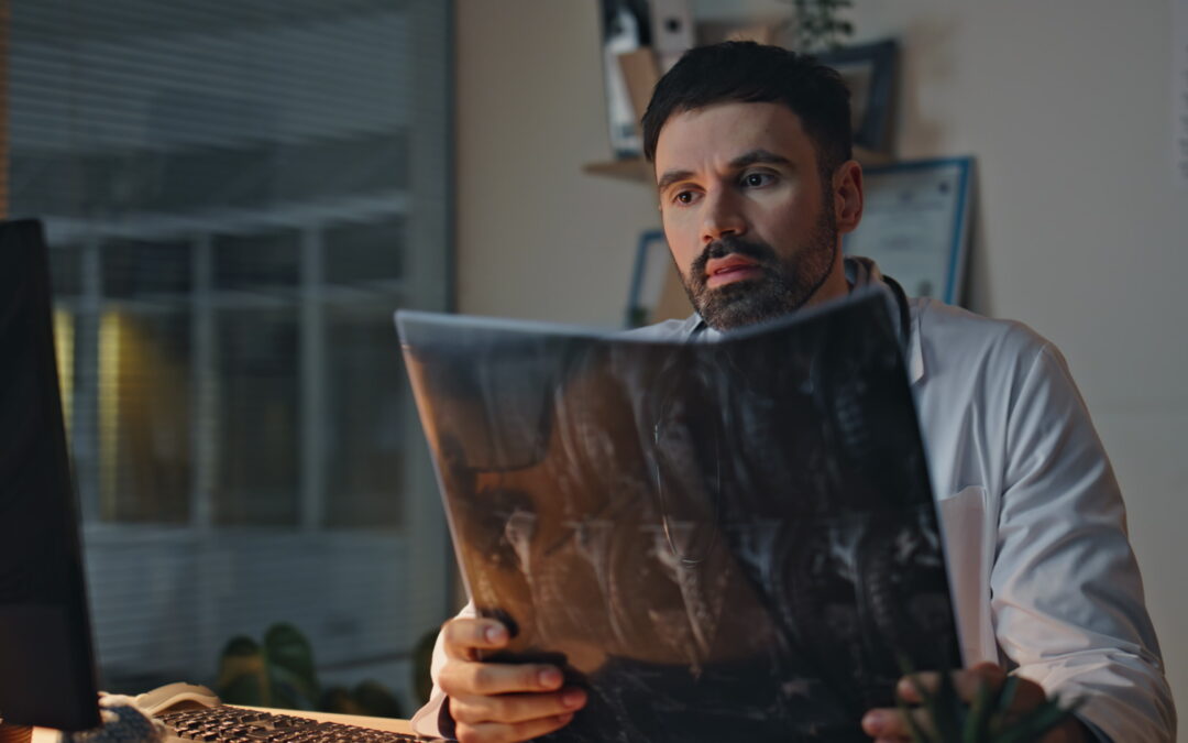 Upset medical expert looking radiology scan at night. Closeup bearded therapist checking x-ray feeling despair in health center. Tired healthcare worker in white coat studying image diagnosis in clinic.